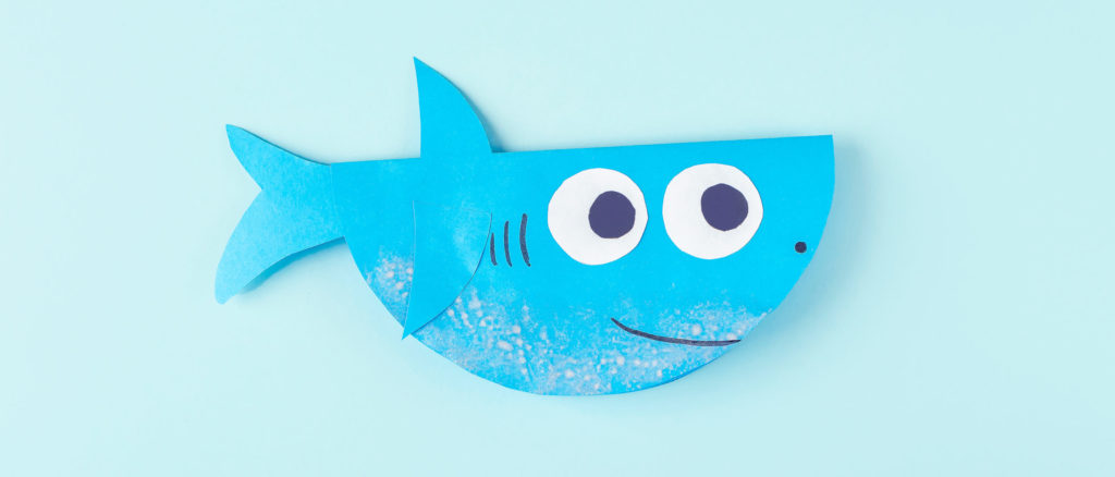 Happy blue construction paper shark on a light blue background
